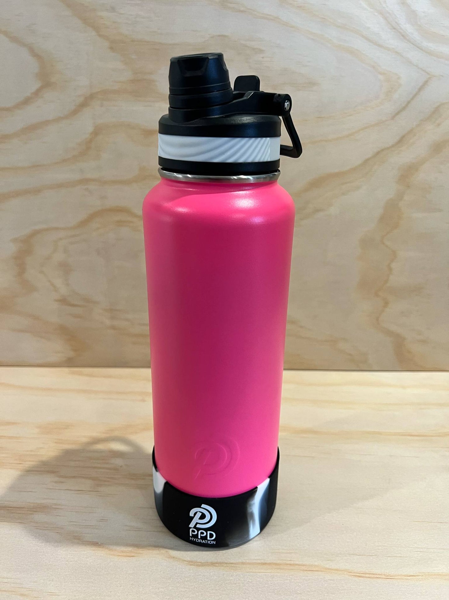 Pink water bottle with black cap on a wooden surface