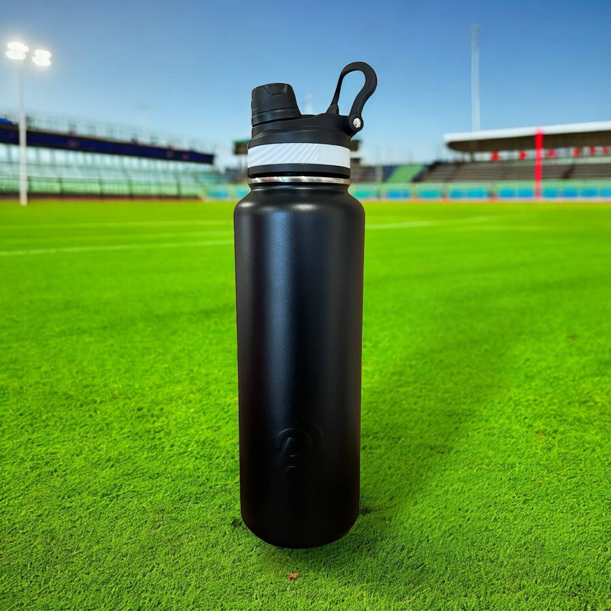 Black water bottle on a grassy field with stadium lights in the background