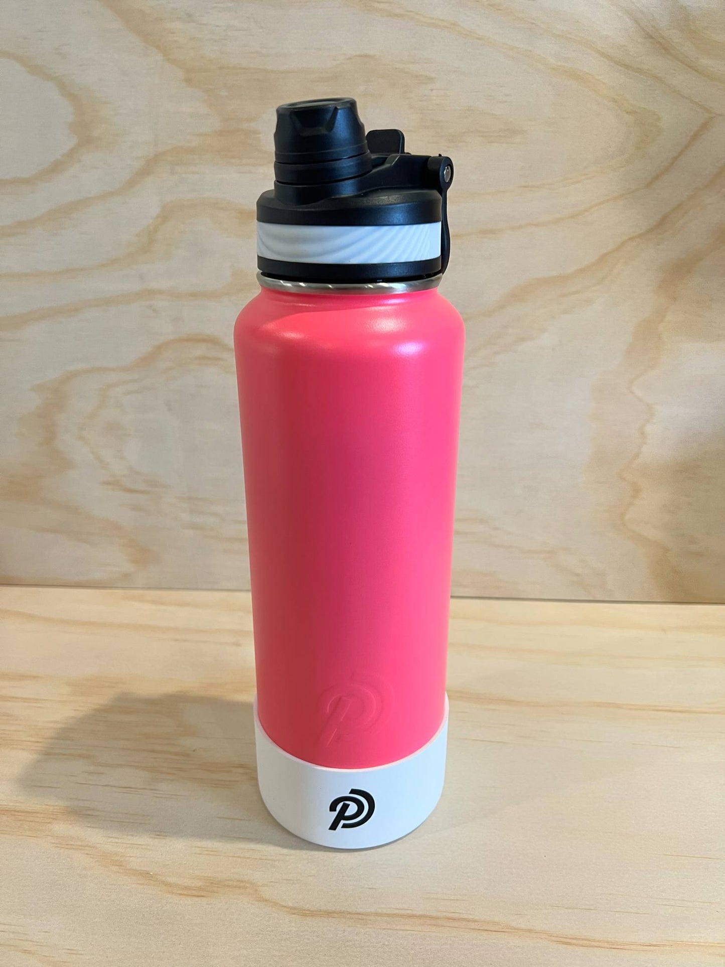 Pink water bottle with black cap on a wooden surface
