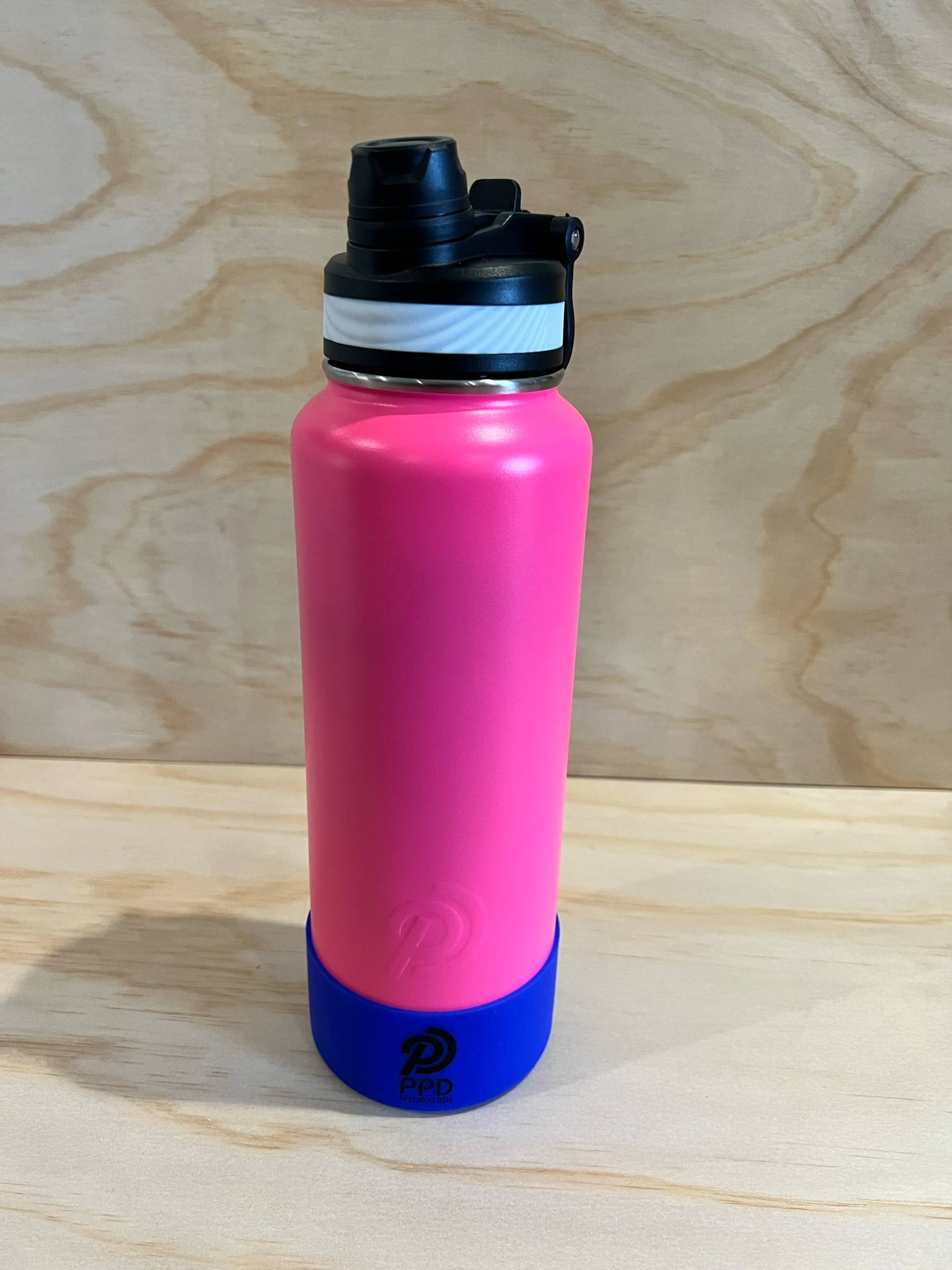 Pink water bottle with black cap and blue base on a wooden surface