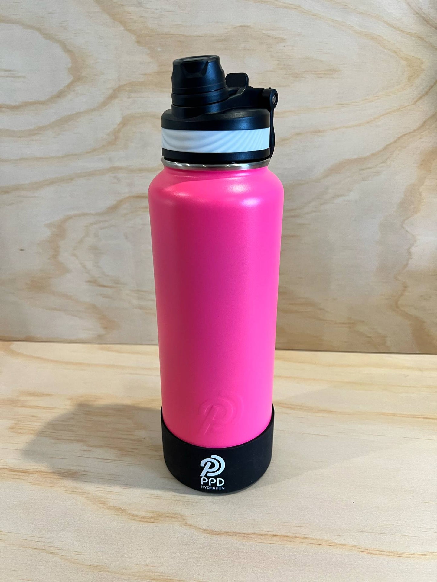 Pink water bottle with black lid on a wooden surface