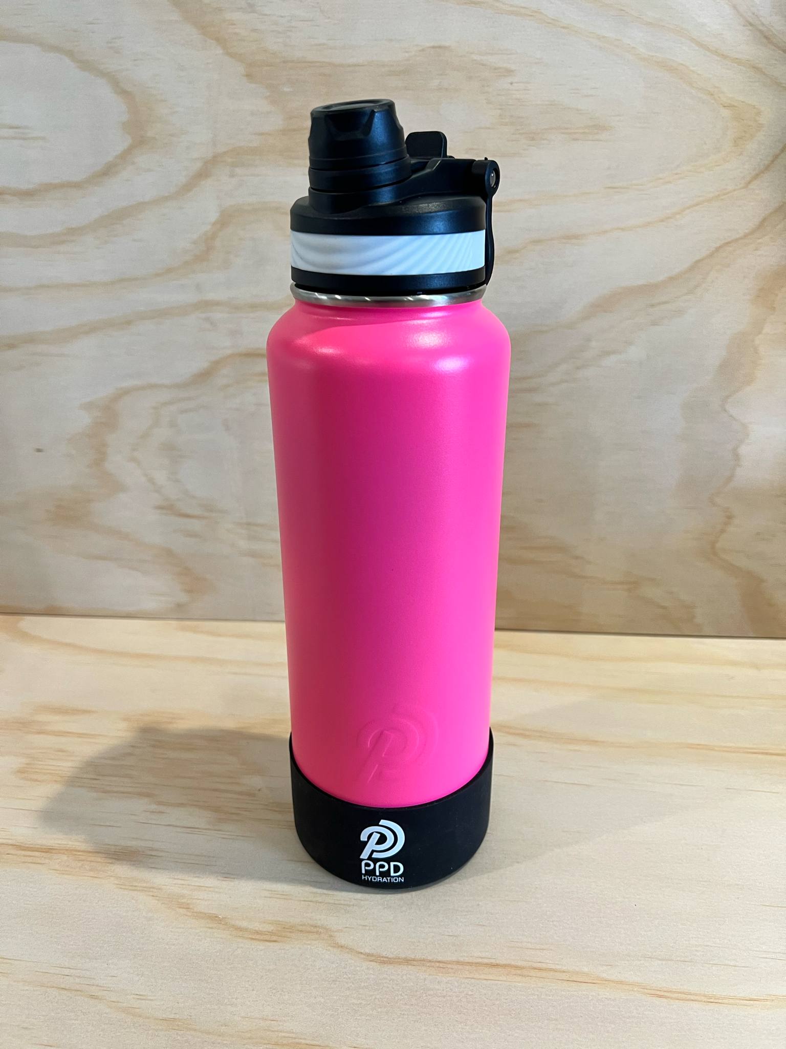 Pink water bottle with black lid on a wooden surface