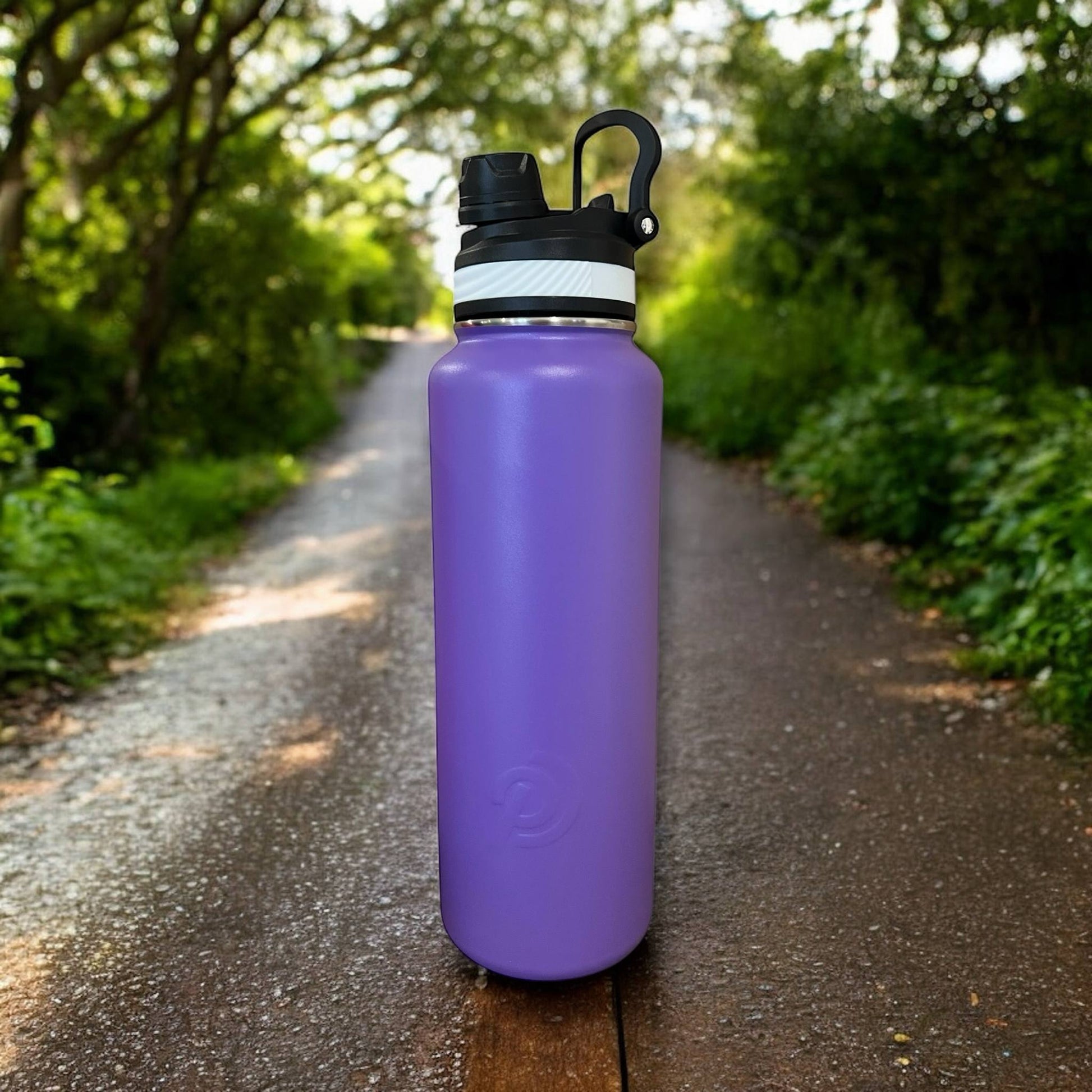 Purple water bottle with black cap on a forest path