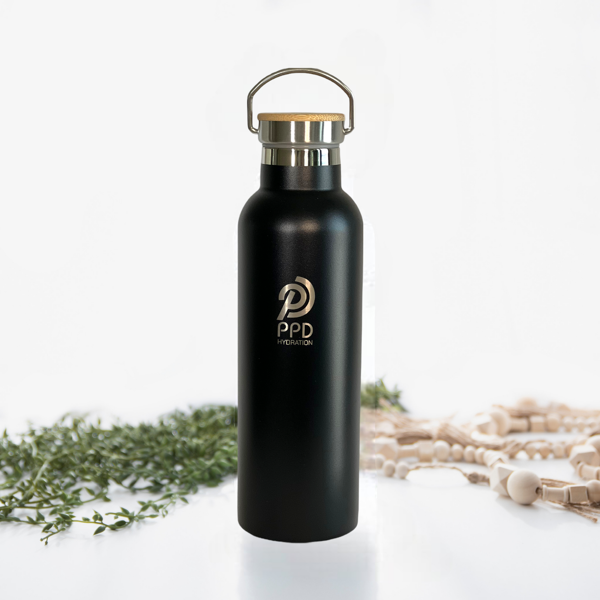 A black stainless steel insulated water bottle with a bamboo lid and a handle at the top. The bottle has a logo printed on it and is displayed alongside a bamboo bumper.