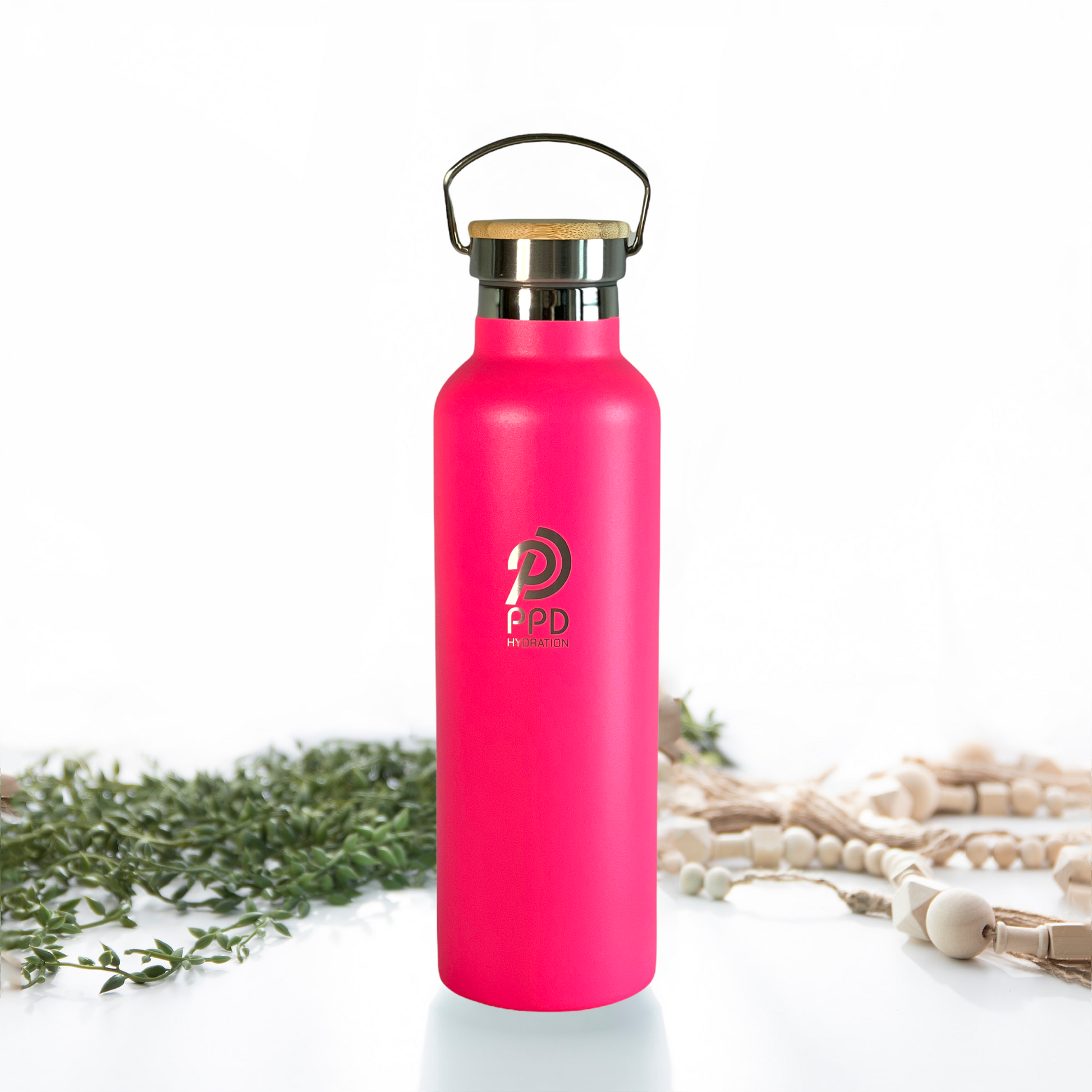 A hot pink stainless steel insulated water bottle with a bamboo lid and a handle at the top. The bottle is displayed alongside some decorative elements, possibly for a product shoot.